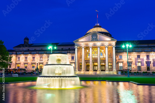 Germany, Ancient Wiesbaden Kurhaus building behind lighted fountain in blue hour mood