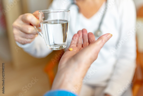Pflegekraft reicht Rentnerin ein Glas Wasser f  r die Medikamente