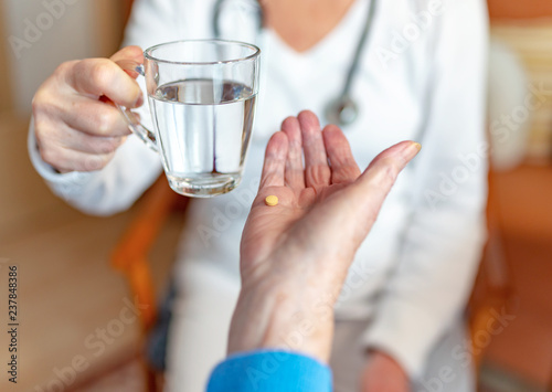 Pflegekraft reicht Rentnerin ein Glas Wasser für die Medikamente