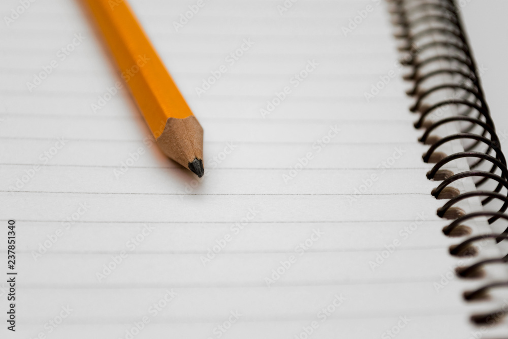 Graphite of yellow pencil on the background of a lined sheet of notebook on a spiral close-up. Copy space Graphite of yellow pencil on the background of a lined sheet of notebook on a spiral close-up. Copy space
