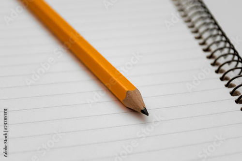 Yellow pencil on the background of a lined sheet of notebook on a spiral close-up and copy space