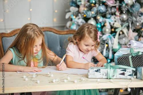 Children little girls sisters with gifts happy fashionable beautiful in Christmas interior write a letter to Santa