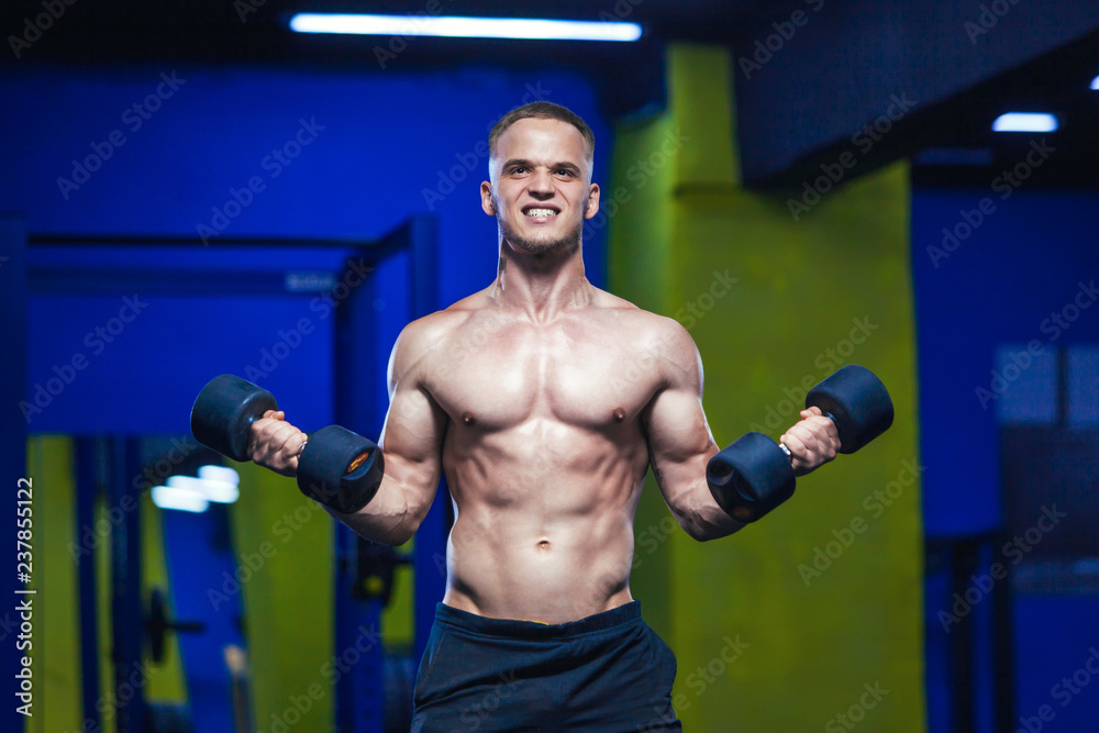 Powerful man doing exercises with dumbbells. Photo of sporty muscular male in the gym. Strength and motivation