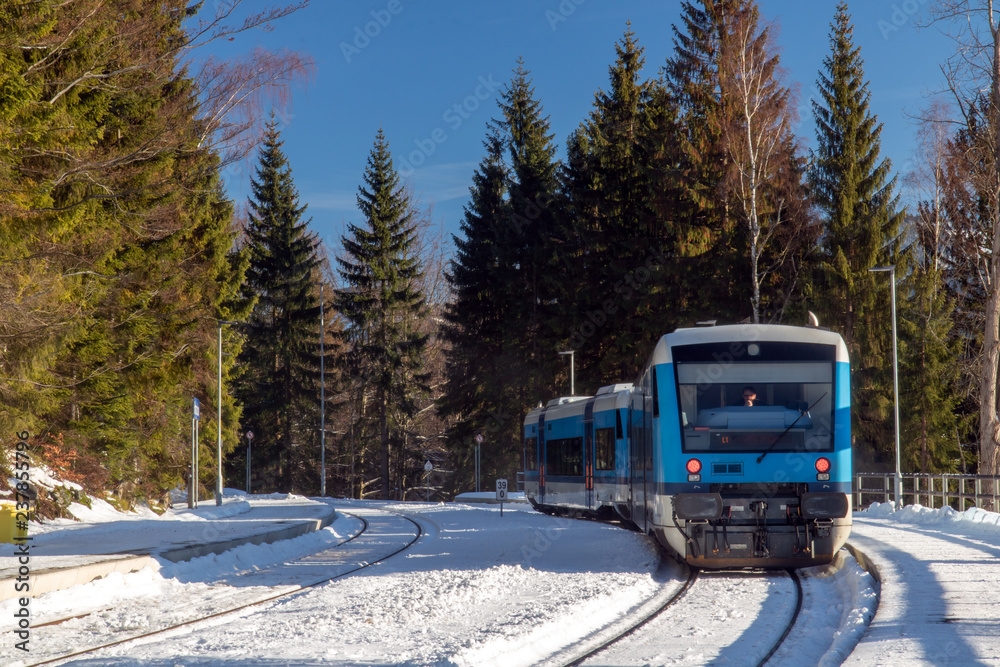 Fototapeta premium Śnieżna stacja kolejowa z nowożytnym pociągiem w górach. Pusta platforma z pociągiem regionalnym w zimowej przyrodzie. Harrachov, Góry Karkonosze, Republika Czeska.