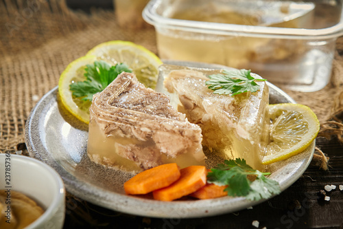 slices of meat jelly with carrots and lemon in a plate on a on sackcloth wooden table. Free space for text.close-up