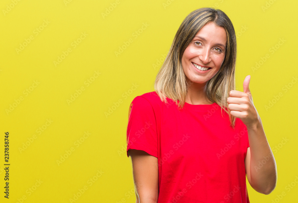 Young beautiful woman over isolated background doing happy thumbs up gesture with hand. Approving expression looking at the camera with showing success. Young beautiful woman over isolated background doing happy thumbs up gesture with hand. Approving expression looking at the camera with showing success.
