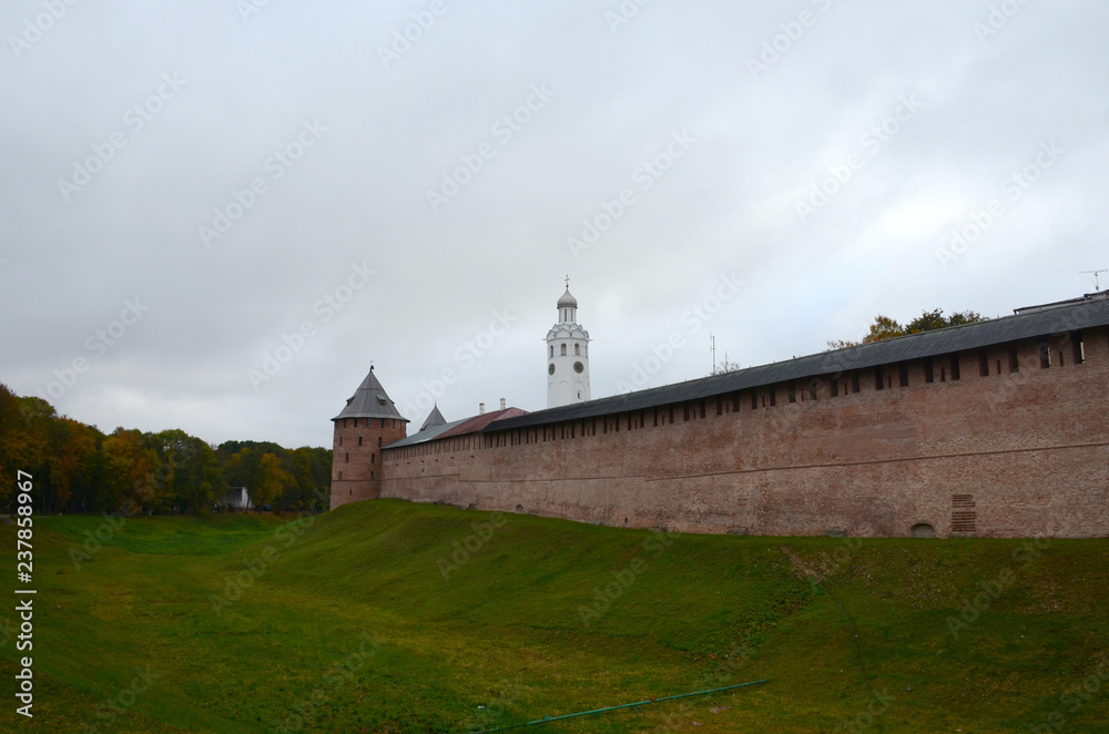Red wall of the Kremlin with a corner tower next to a moat covered with grass. Veliky Novgorod, Russia.