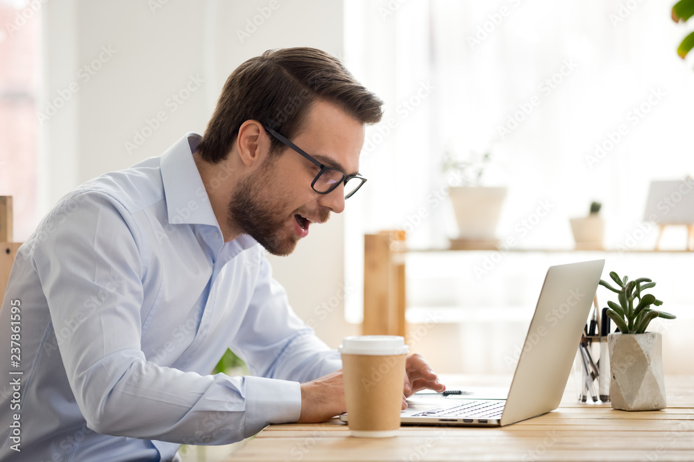 Excited male worker look at laptop screen reading breaking news, surprised man using computer get unexpected email offer or promotion letter, lucky employee feel euphoric win lottery online Excited male worker look at laptop screen reading breaking news, surprised man using computer get unexpected email offer or promotion letter, lucky employee feel euphoric win lottery online