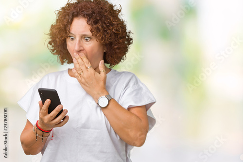 Middle ager senior woman using and texting with smartphone over isolated background cover mouth with hand shocked with shame for mistake, expression of fear, scared in silence, secret concept