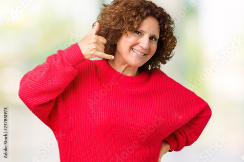 Beautiful middle ager senior woman red winter sweater over isolated background smiling doing phone gesture with hand and fingers like talking on the telephone. Communicating concepts.