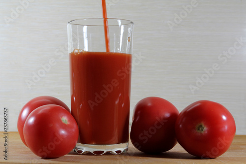 Fresh tomato juice is poured into a glass. Nearby are red tomatoes.