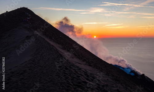 Bild auf Leinwand Summit of mount Stromboli at sunset with smoke, a group of tourists and the Mediterranean Sea in the background