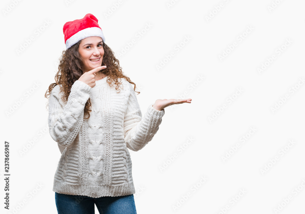 Young brunette girl wearing christmas hat over isolated background amazed and smiling to the camera while presenting with hand and pointing with finger. Young brunette girl wearing christmas hat over isolated background amazed and smiling to the camera while presenting with hand and pointing with finger.