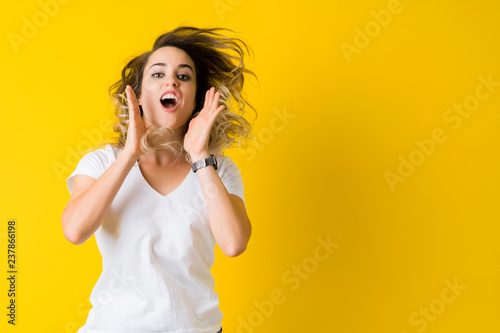 Beautiful young blonde woman jumping happy and surprised over isolated yellow background © Krakenimages.com