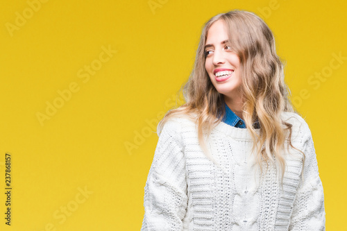 Beautiful young blonde woman wearing winter sweater over isolated background looking away to side with smile on face, natural expression. Laughing confident. © Krakenimages.com