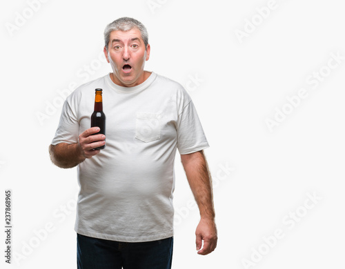 Handsome senior man drinking beer bottle over isolated background scared in shock with a surprise face, afraid and excited with fear expression