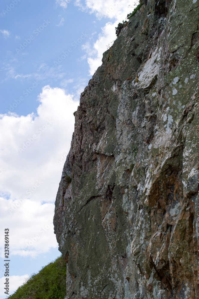 Sheer steep rocky cliff face in Wicklow, Ireland with blue sky and white clouds background Sheer steep rocky cliff face in Wicklow, Ireland with blue sky and white clouds background