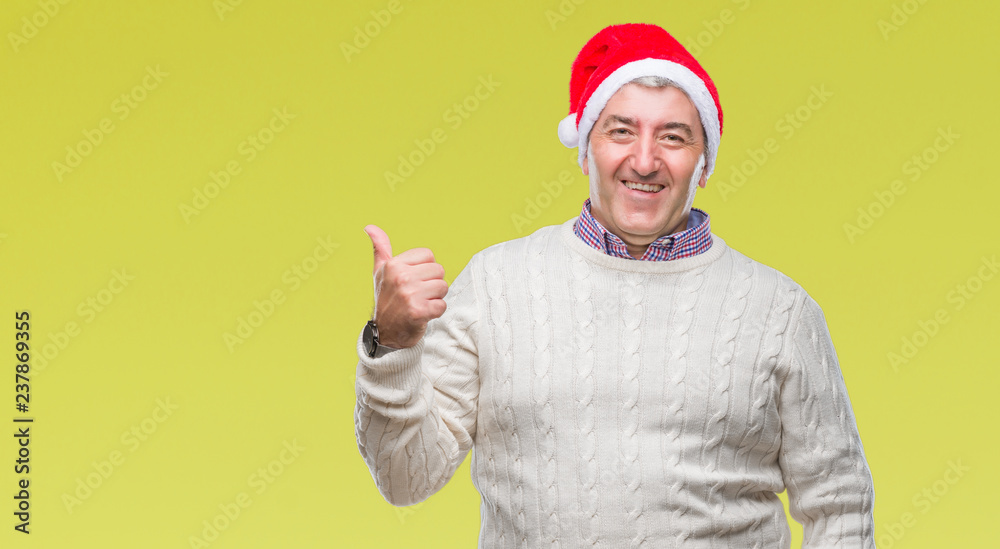 Fototapeta premium Handsome senior man wearing christmas hat over isolated background smiling with happy face looking and pointing to the side with thumb up.