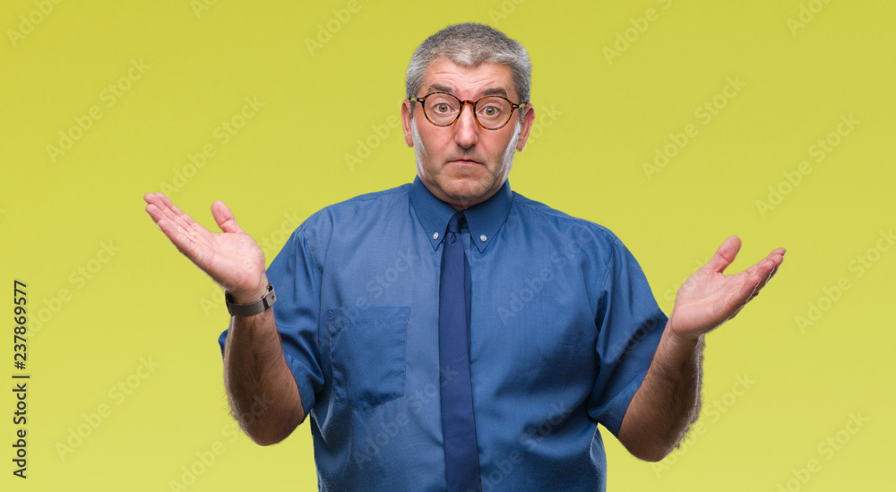 Handsome senior business man over isolated background clueless and confused expression with arms and hands raised. Doubt concept.