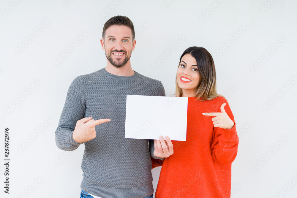 Young couple holding blank sheet paper over isolated background very happy pointing with hand and finger - obrazy, fototapety, plakaty 