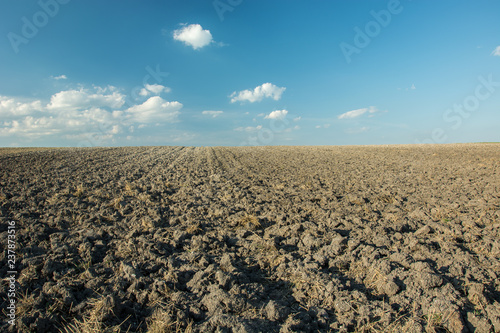 Large plowed field and white clouds on blue sky