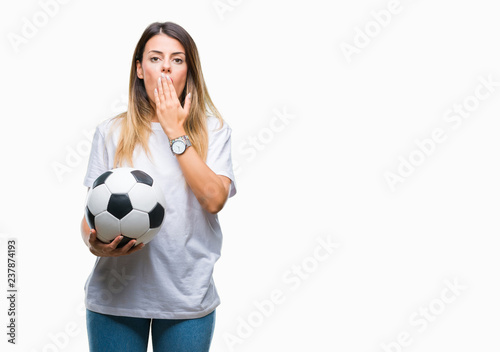 Young beautiful woman holding soccer ball over isolated background cover mouth with hand shocked with shame for mistake, expression of fear, scared in silence, secret concept