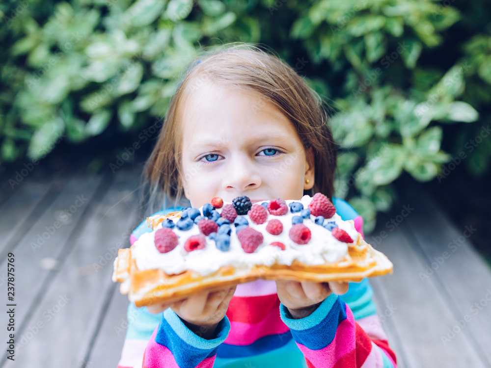 waffles - girl eating a waffle with whipped cream, raspberries and blueberries outdoors  in the garden smiling