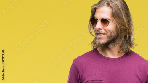 Young handsome man with long hair wearing sunglasses over isolated background looking away to side with smile on face, natural expression. Laughing confident.