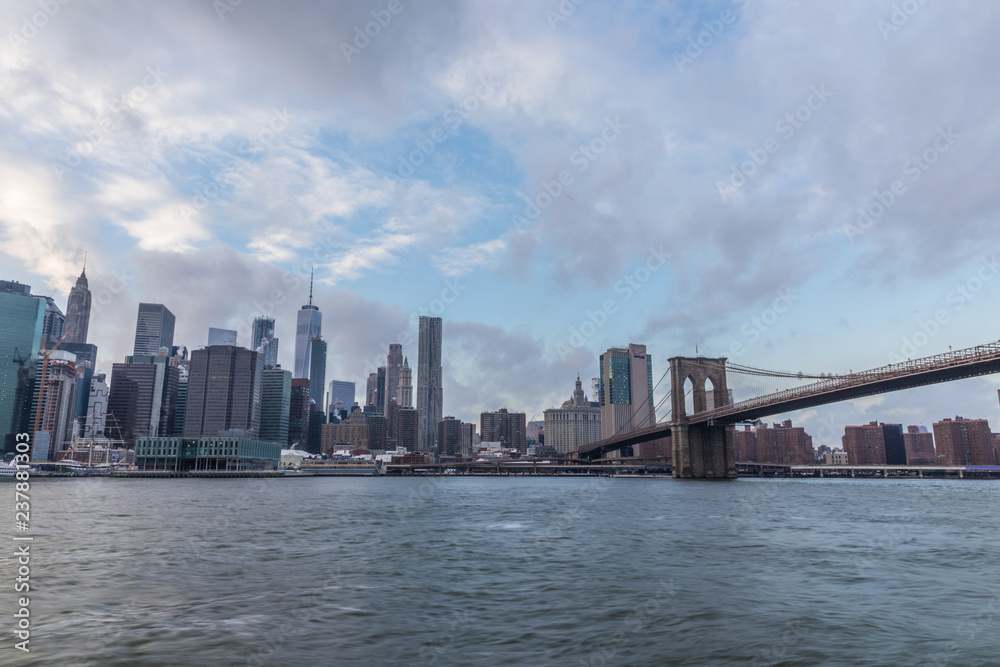 View of Manhattan with Brooklyn Bridge at sunset from the side of the pier.