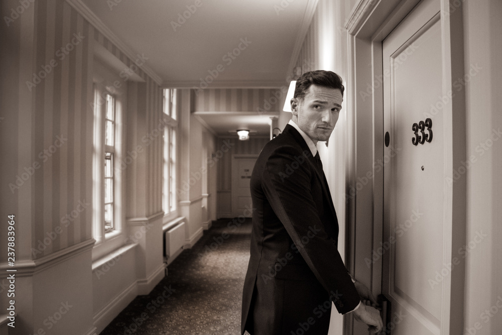Sepia image of handsome man in suit in hotel corridor using key card to open room door Sepia image of handsome man in suit in hotel corridor using key card to open room door