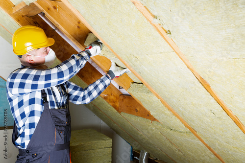 Man installing thermal roof insulation layer - using mineral wool panels. Attic renovation and insulation concept