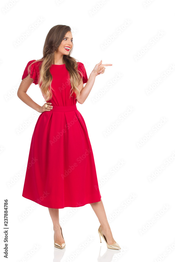 Smiling Fashion Woman In Red Dress And Gold High Heels Is Looking Away And Pointing Smiling Fashion Woman In Red Dress And Gold High Heels Is Looking Away And Pointing