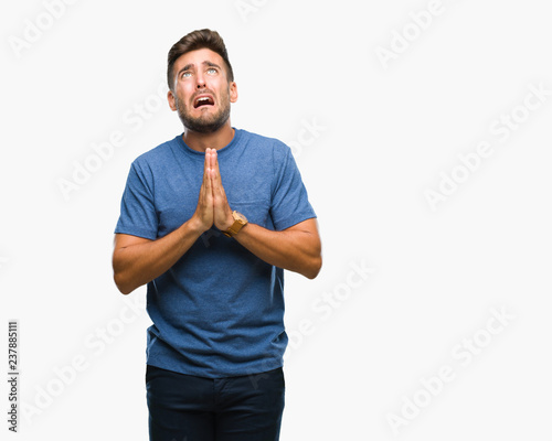 Young handsome man over isolated background begging and praying with hands together with hope expression on face very emotional and worried. Asking for forgiveness. Religion concept.