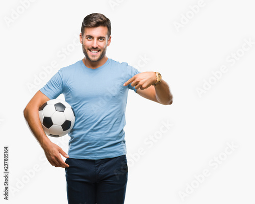 Young handsome man holding soccer football ball over isolated background with surprise face pointing finger to himself