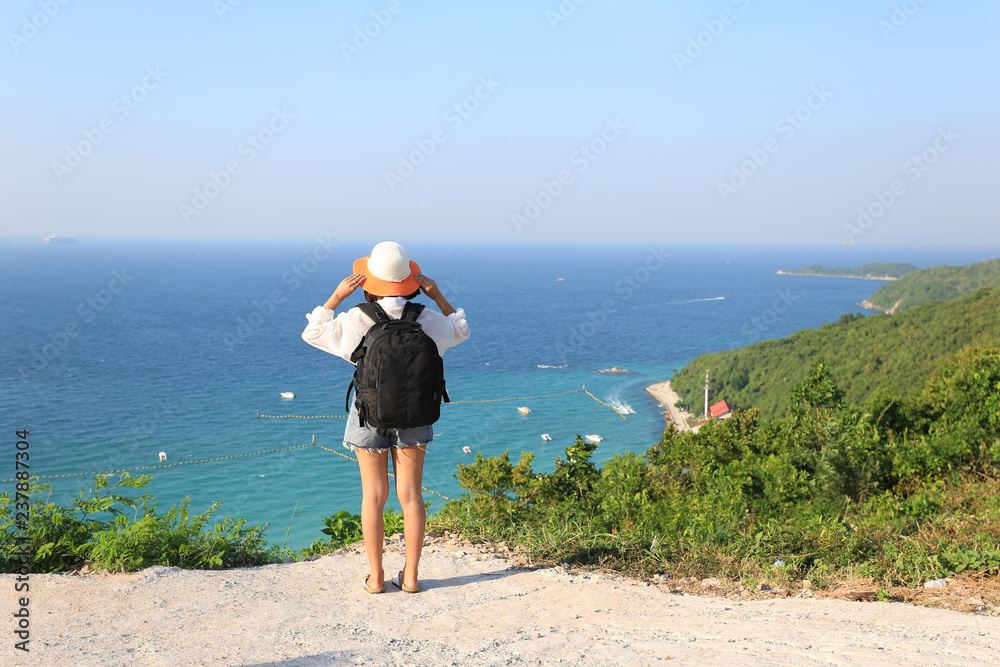 Young woman traveler with backpack enjoying and standing on mountains of the sea background, Koh Larn in Pattaya city, Chonburi Thailand