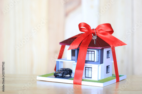 Real estate and Gift new home concept,Model house with Red ribbon and key on wooder background photo