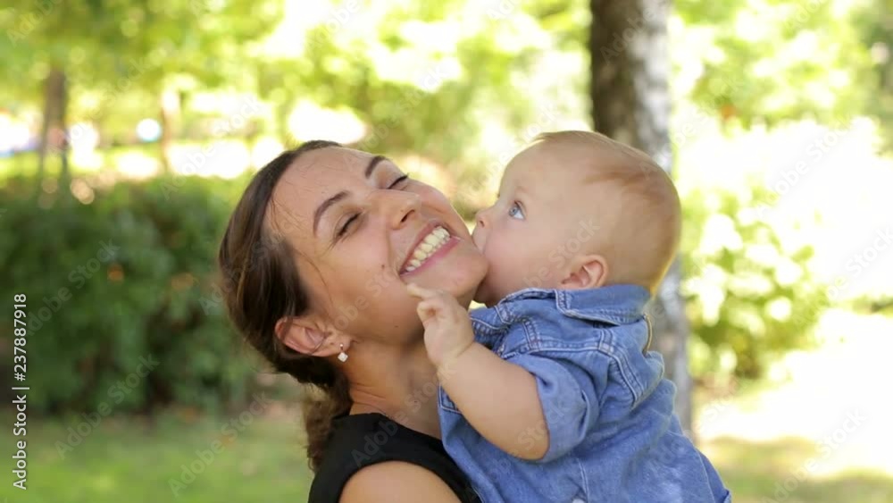Close-up of a mother hugging her five-month-old son in a summer park. Portrait of a young mother with a child in the park, the baby tightly hugs his mom. Close-up of a mother hugging her five-month-old son in a summer park. Portrait of a young mother with a child in the park, the baby tightly hugs his mom.