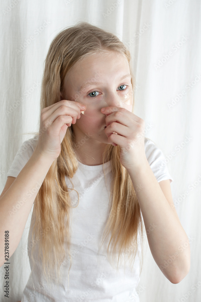 Young girl with curly and blonde hair trying on her mother's moisturizing patches from edema and tired eyes. Isolated photo on white background. Young girl with curly and blonde hair trying on her mother's moisturizing patches from edema and tired eyes. Isolated photo on white background.