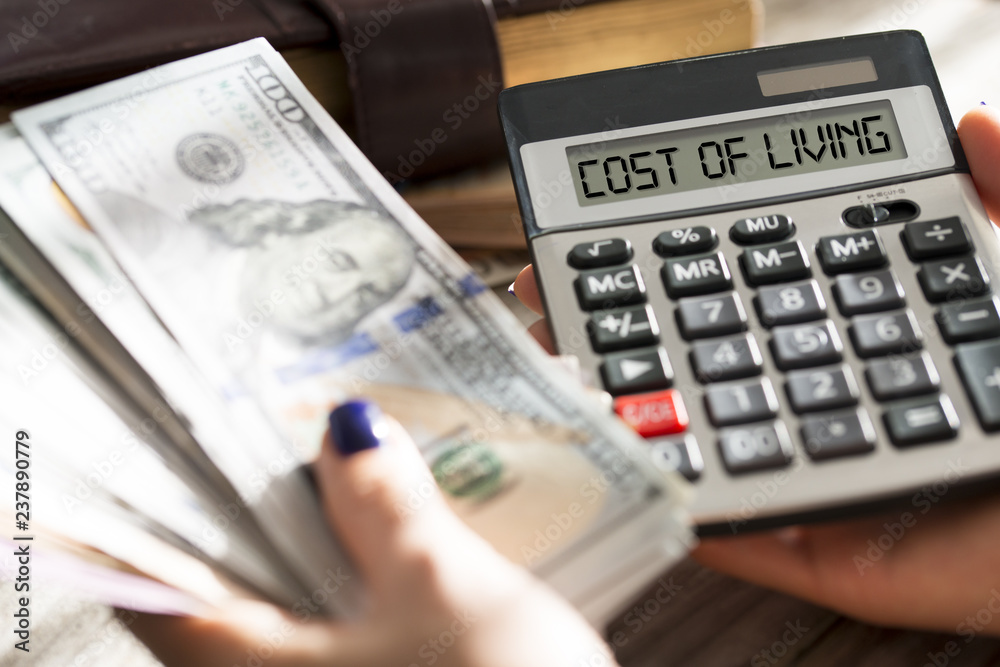 Fototapeta premium Woman calculating cost of living with calculator cash us dollar banknotes