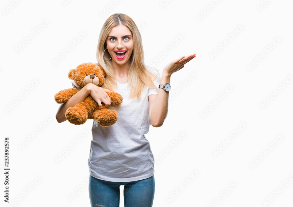Young beautiful blonde woman holding teddy bear over isolated background very happy and excited, winner expression celebrating victory screaming with big smile and raised hands Young beautiful blonde woman holding teddy bear over isolated background very happy and excited, winner expression celebrating victory screaming with big smile and raised hands