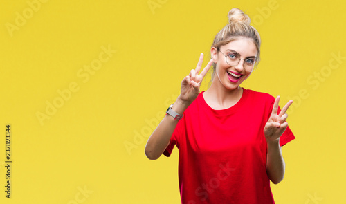 Young beautiful blonde woman wearing red t-shirt and glasses over isolated background smiling looking to the camera showing fingers doing victory sign. Number two.