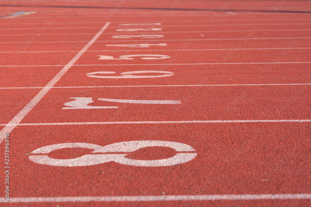 White numbers on starting line of a running track field, 1-8, with straight white lines divided each track equally.