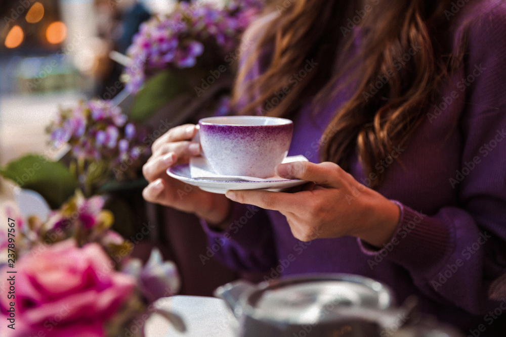 Close-up of a woman who is sitting in the restaurant outdoor and holding a cup of tea Close-up of a woman who is sitting in the restaurant outdoor and holding a cup of tea