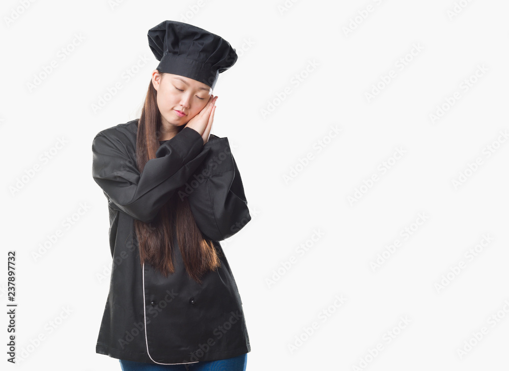 Young Chinese woman over isolated background wearing chef uniform sleeping tired dreaming and posing with hands together while smiling with closed eyes. Young Chinese woman over isolated background wearing chef uniform sleeping tired dreaming and posing with hands together while smiling with closed eyes.