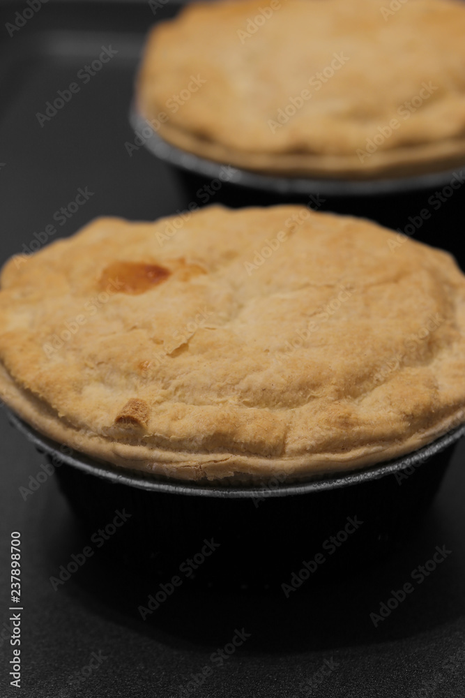 Individual steak pies in foil with a pastry topping on a baking tray Individual steak pies in foil with a pastry topping on a baking tray