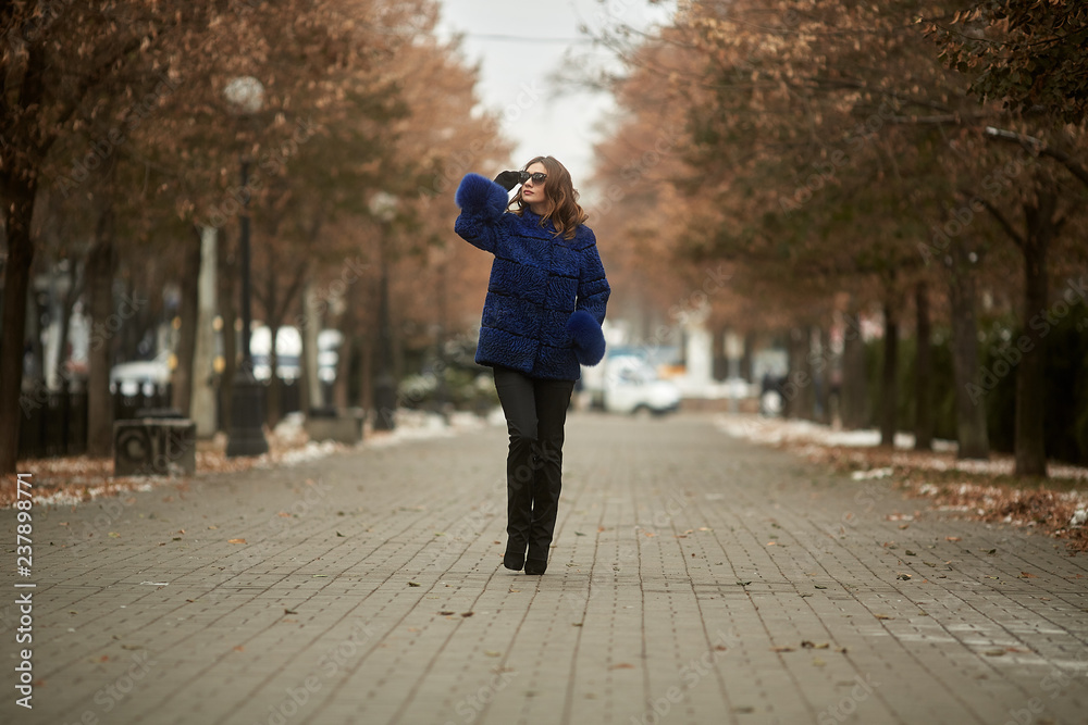 The girl walks through the city in a fur coat