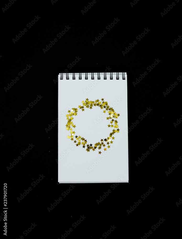 Spiral Notebook, realistic mockup White scetchbook on black abstract background with golden stars confetti.Vrtical l top view..
