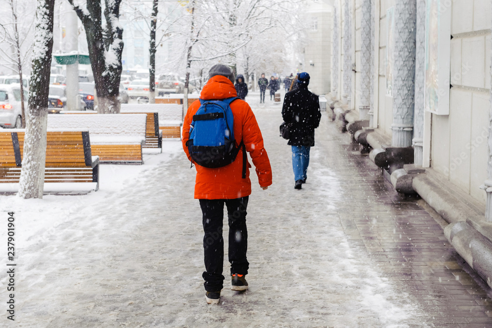 Fototapeta premium Winter, city, December, it is snowing, a man walking down the street, rear view