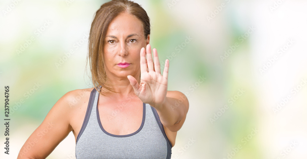 Beautiful middle age woman wearing sport clothes over isolated background doing stop sing with palm of the hand. Warning expression with negative and serious gesture on the face. Beautiful middle age woman wearing sport clothes over isolated background doing stop sing with palm of the hand. Warning expression with negative and serious gesture on the face.