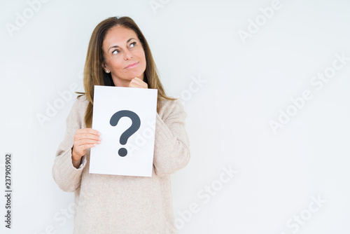 Middle age woman thinking and holding paper with question mark symbol over isolated background serious face thinking about question, very confused idea